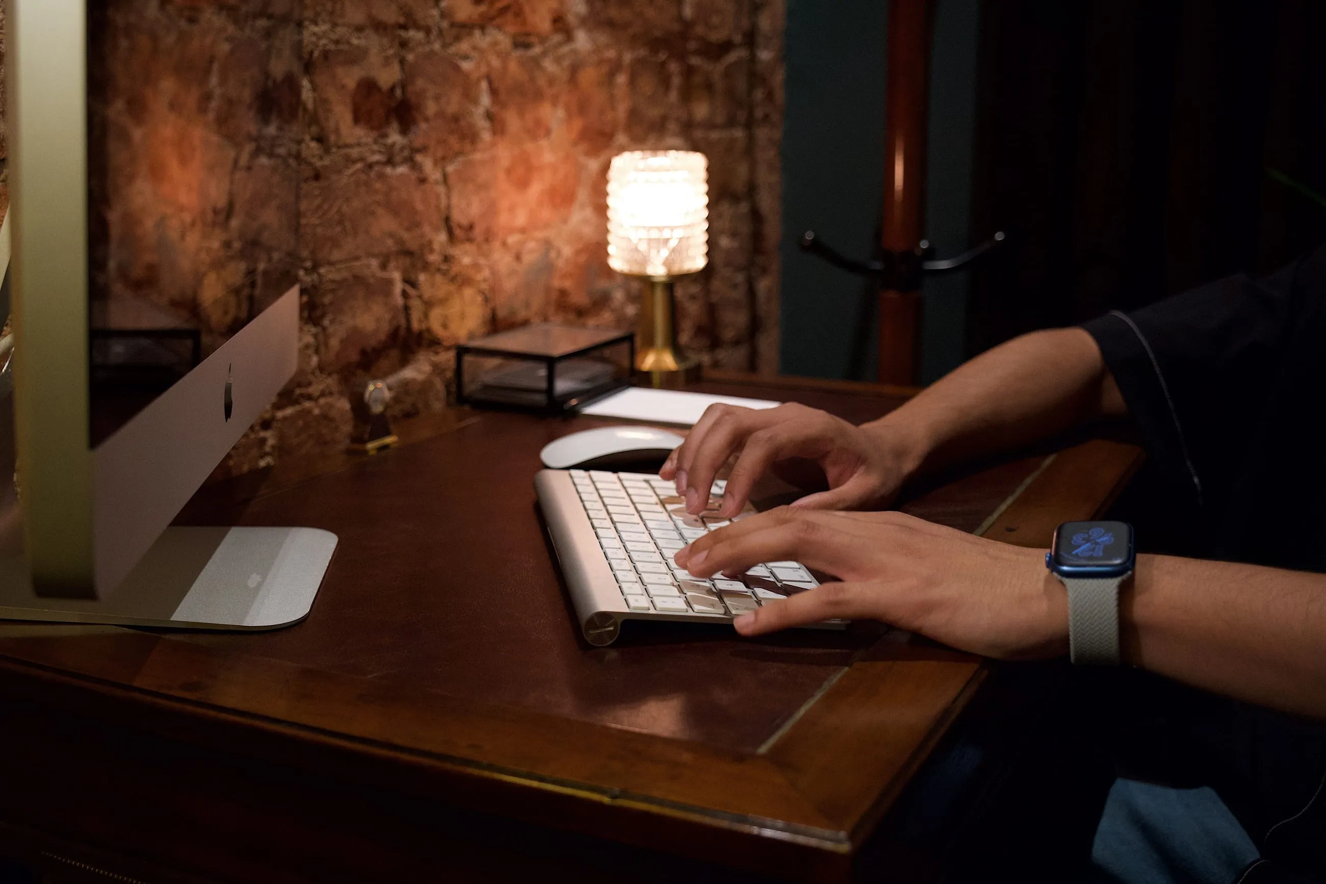 Escritorio de madera de noche: manos sobre el teclado bajo una lámpara cálida